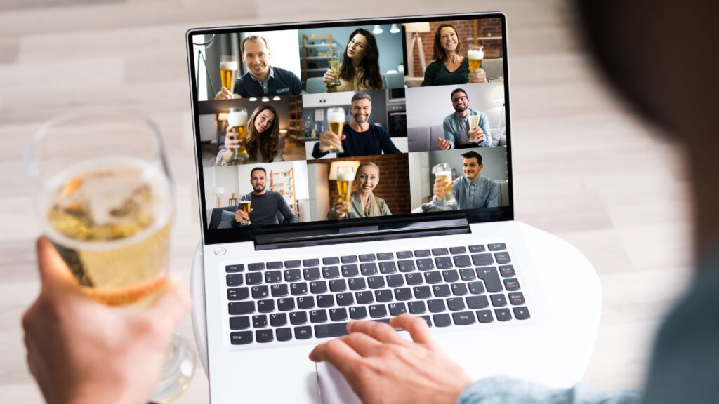 person holding a drink while attending a virtual party on a laptop
