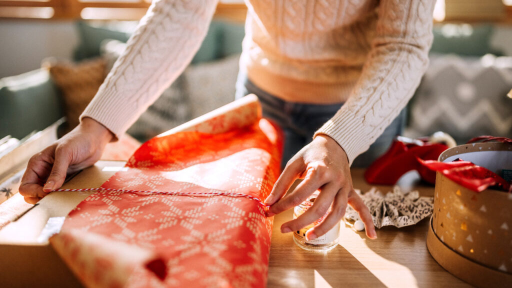 person wrapping a gift with red festive paper